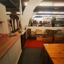 Winkelinterieur met houten meubels, fauteuils en diverse huishoudartikelen langs rode vloerbedekking