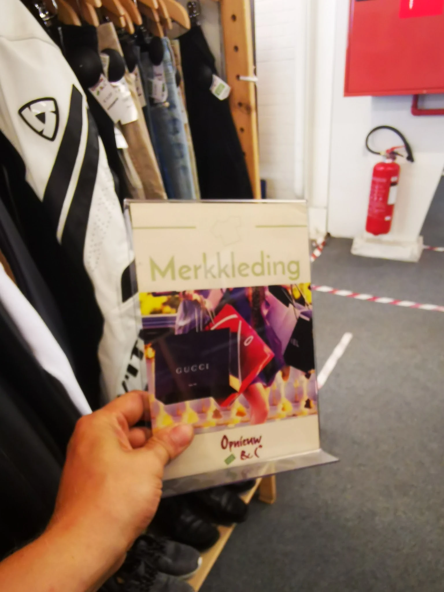 Hand met een merkkleding-catalogus of brochure met Gucci-afbeelding, in een kringloopwinkel