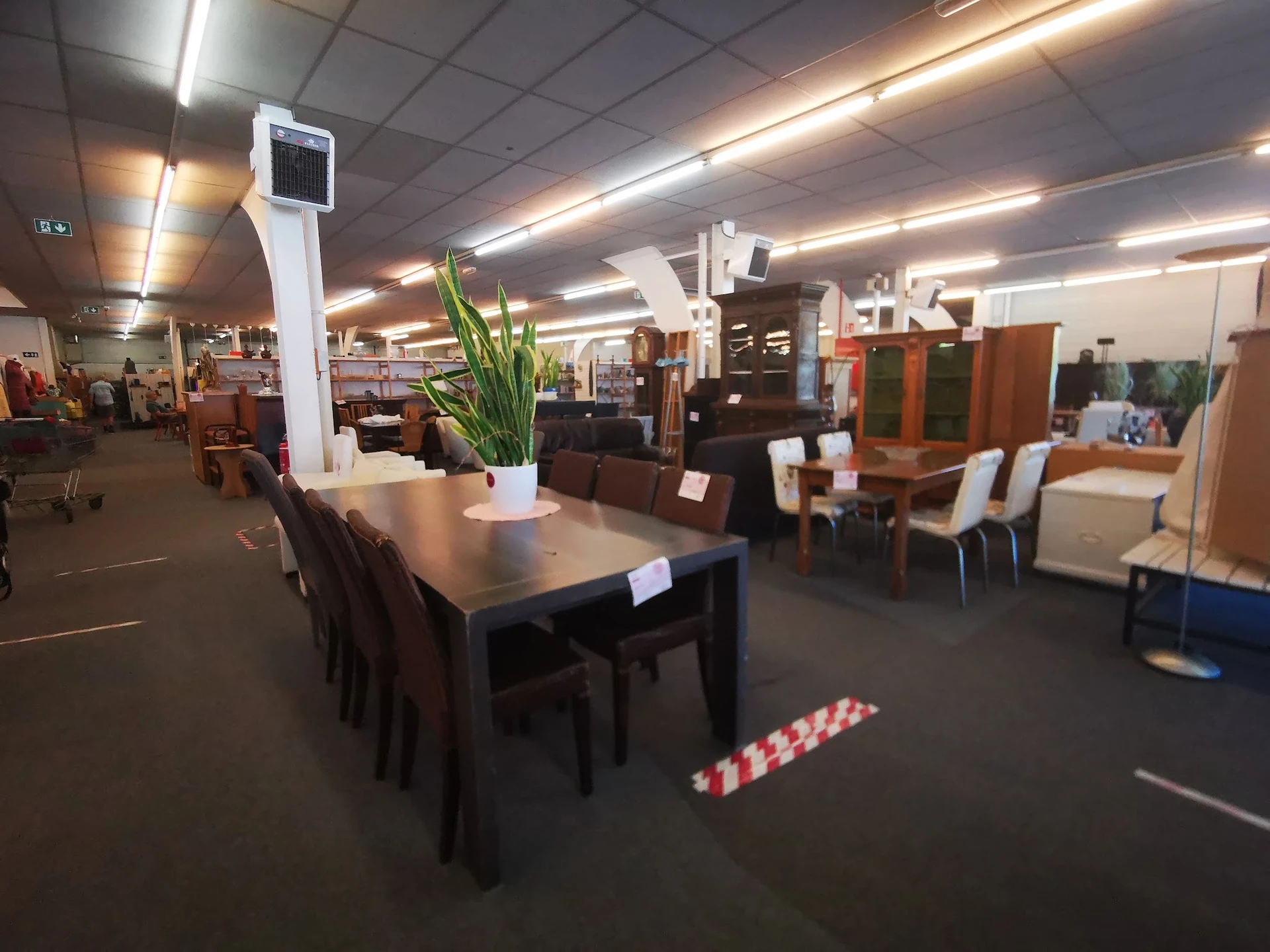 Winkelvloer met tafel en stoelen, diverse meubels en kasten op de achtergrond, fluorescerende plafondverlichting