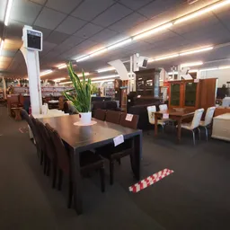 Winkelvloer met tafel en stoelen, diverse meubels en kasten op de achtergrond, fluorescerende plafondverlichting