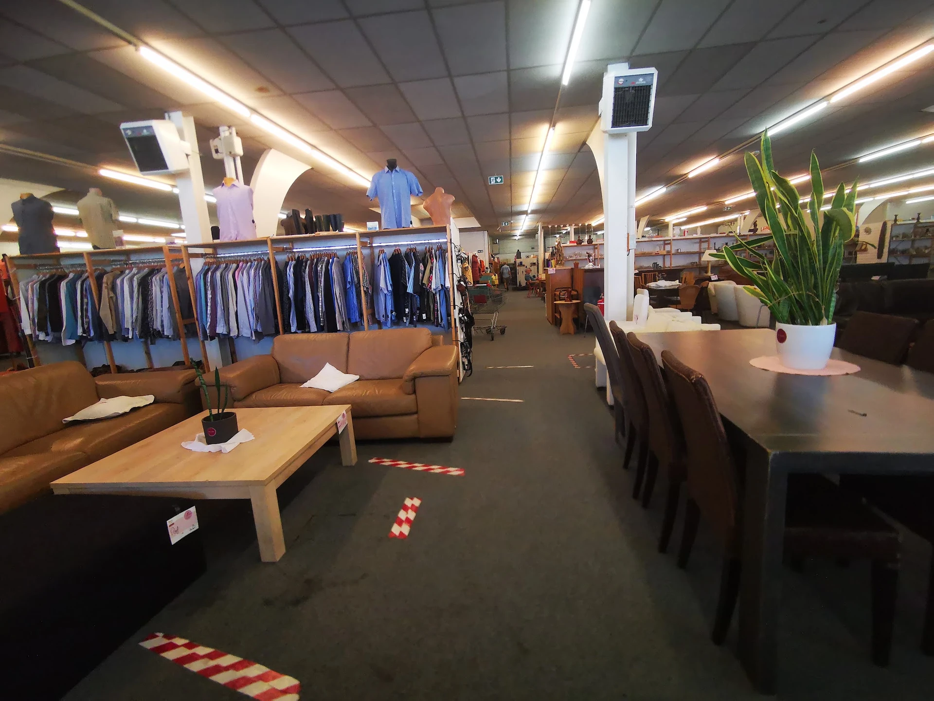 Winkelvloer met kledingrekken, zithoeken en tafels in kringloopwinkel
