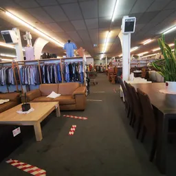Winkelvloer met kledingrekken, zithoeken en tafels in kringloopwinkel