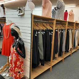 Houten rekken met uitgestalde dameskleding, waaronder jurken, broeken en tops in verschillende kleuren. Een mannequin toont e