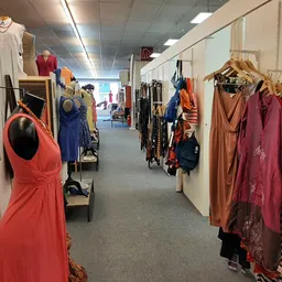 Winkelgang met kledingrekken vol tweedehands kleding in verschillende kleuren, zoals rood, blauw en bruin.