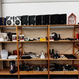 Houten stellingen met diverse gebruikte elektronische apparaten, speakers, camera's en huishoudelijke items