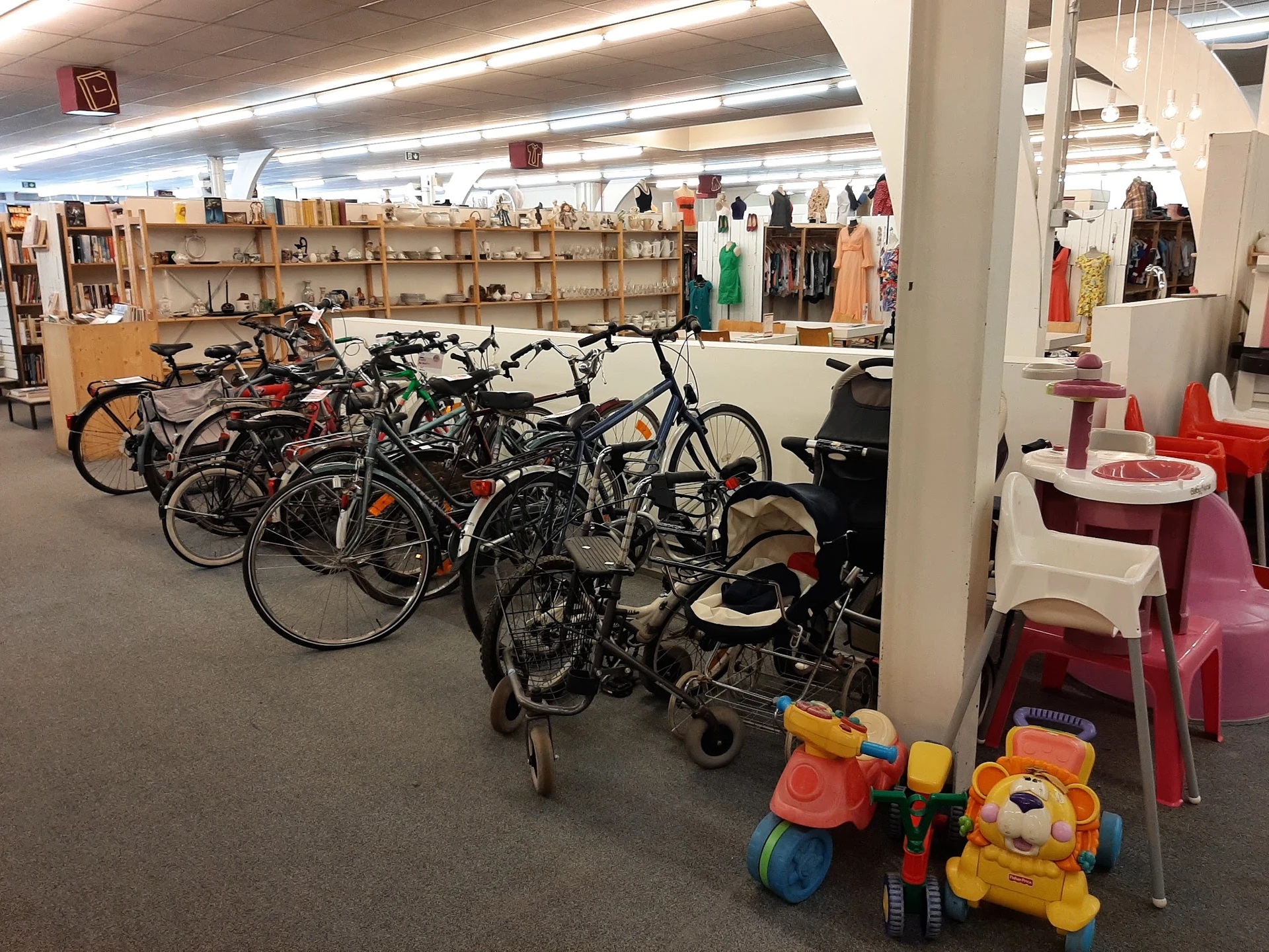 Winkelvloer met fietsen, kinderwagens en speelgoed, stellingen met kleding op achtergrond