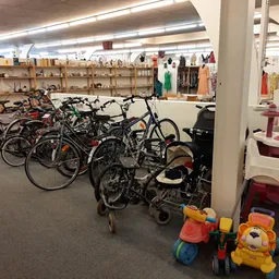 Winkelvloer met fietsen, kinderwagens en speelgoed, stellingen met kleding op achtergrond