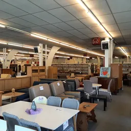 Winkelvloer met zithoeken met grijze stoelen en tafels, houten kastjes en stellingen op de achtergrond