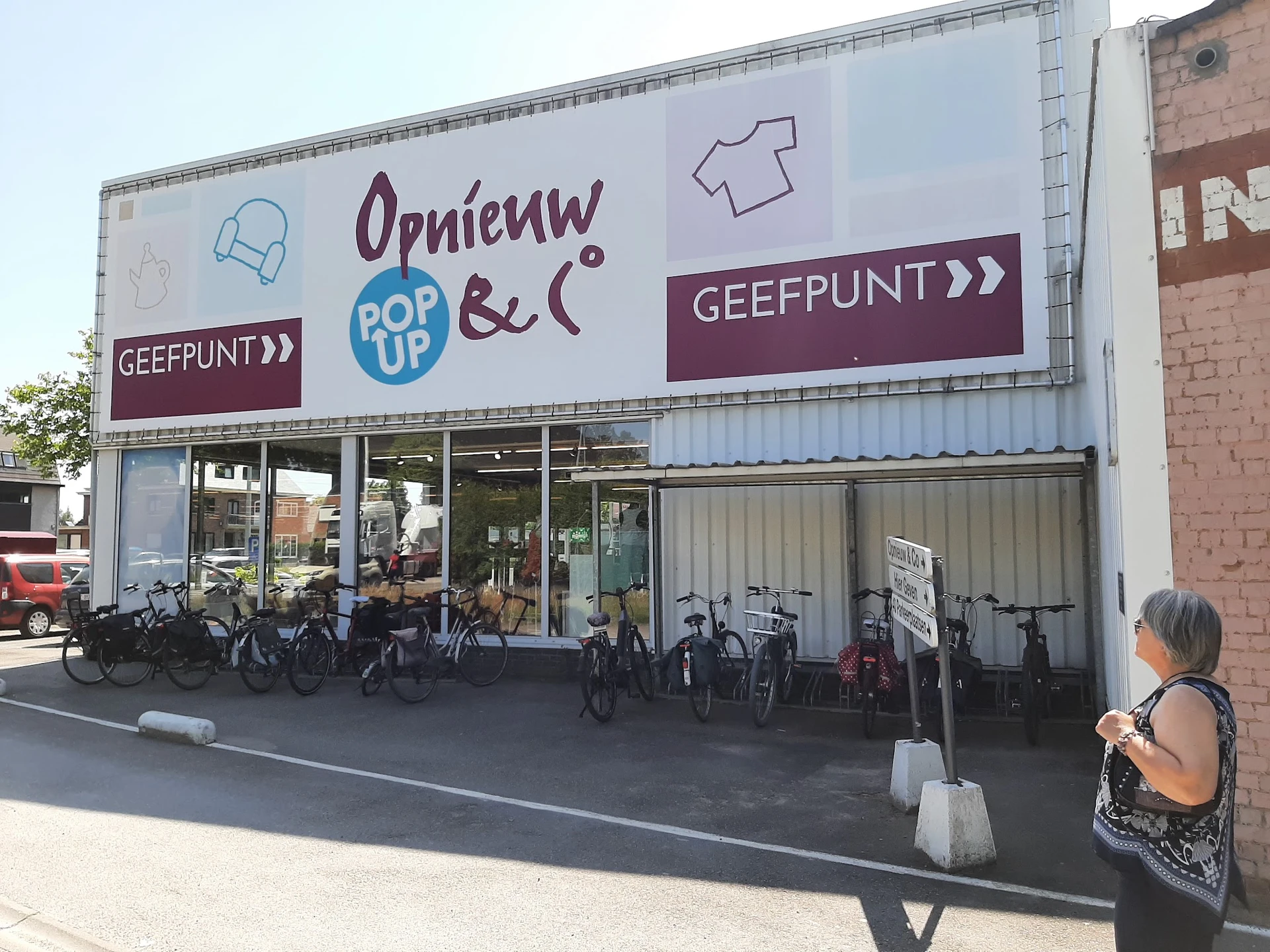 Winkelgevel met groot uithangbord, fietsen geparkeerd ervoor en een vrouw op straat