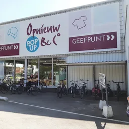 Winkelgevel met groot uithangbord, fietsen geparkeerd ervoor en een vrouw op straat