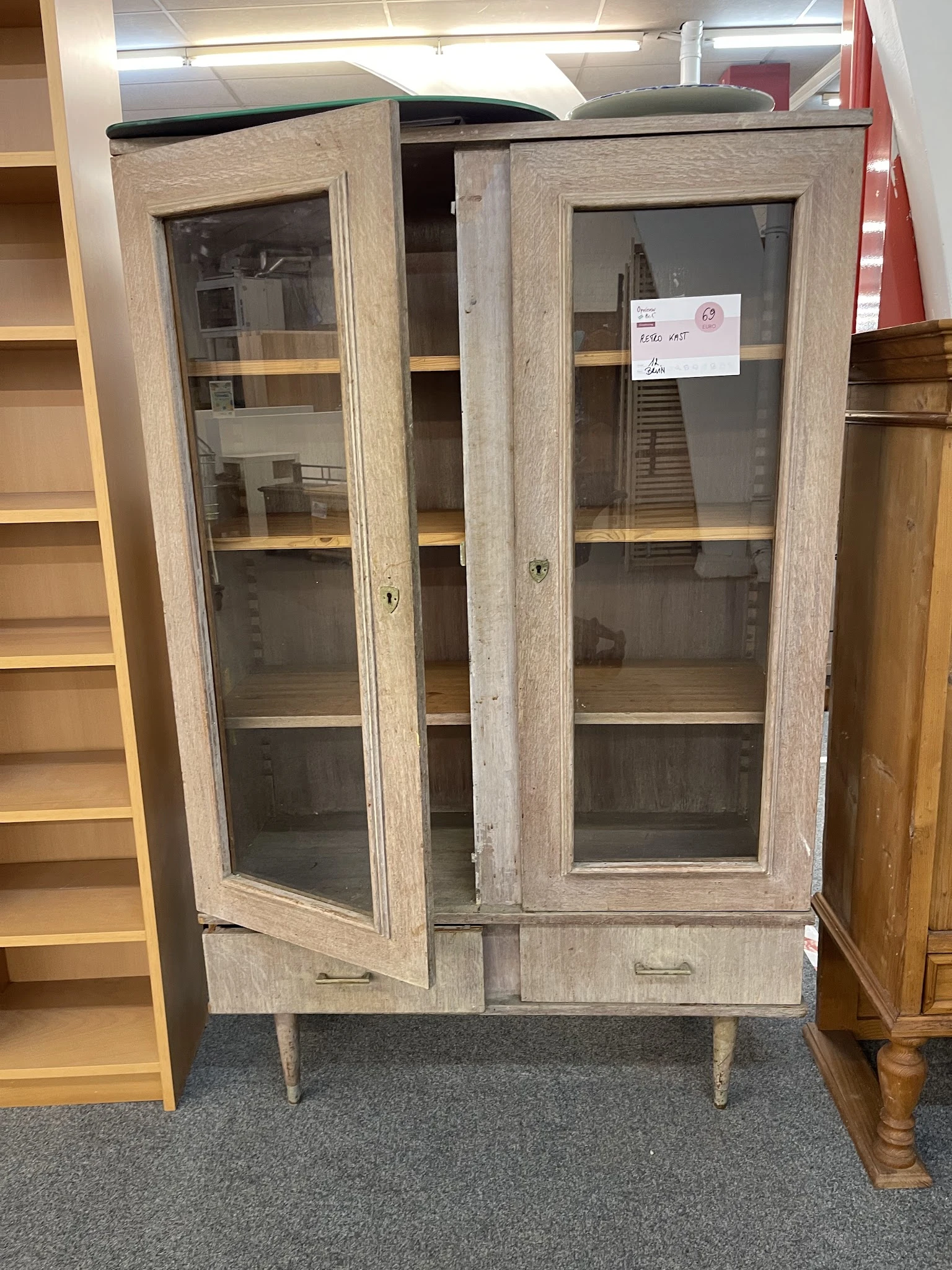 Vintage vitrinekast met houten frame en glazen deuren, met enkele spullen zichtbaar op de planken