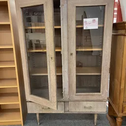 Vintage vitrinekast met houten frame en glazen deuren, met enkele spullen zichtbaar op de planken