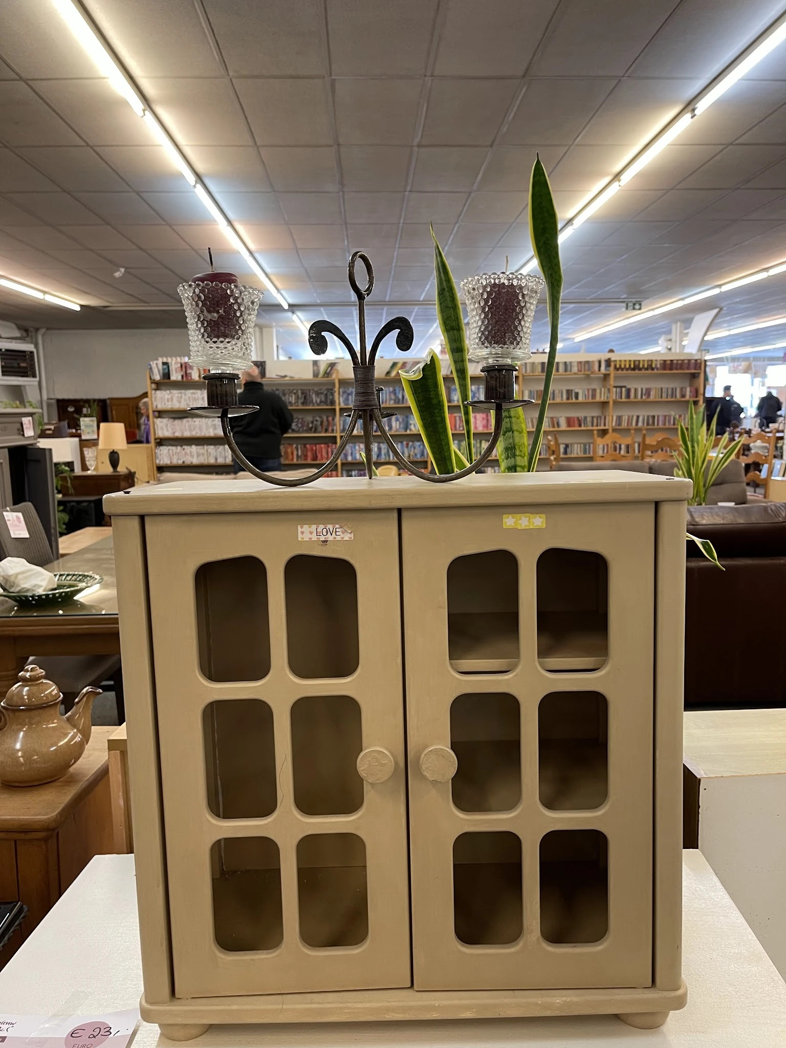 Creme-kleurige kastje met glasdeuren en decoratie op het deksel in een kringloopwinkel