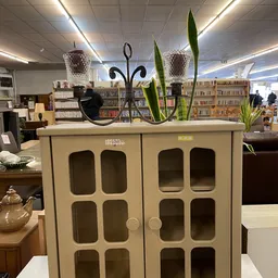 Creme-kleurige kastje met glasdeuren en decoratie op het deksel in een kringloopwinkel