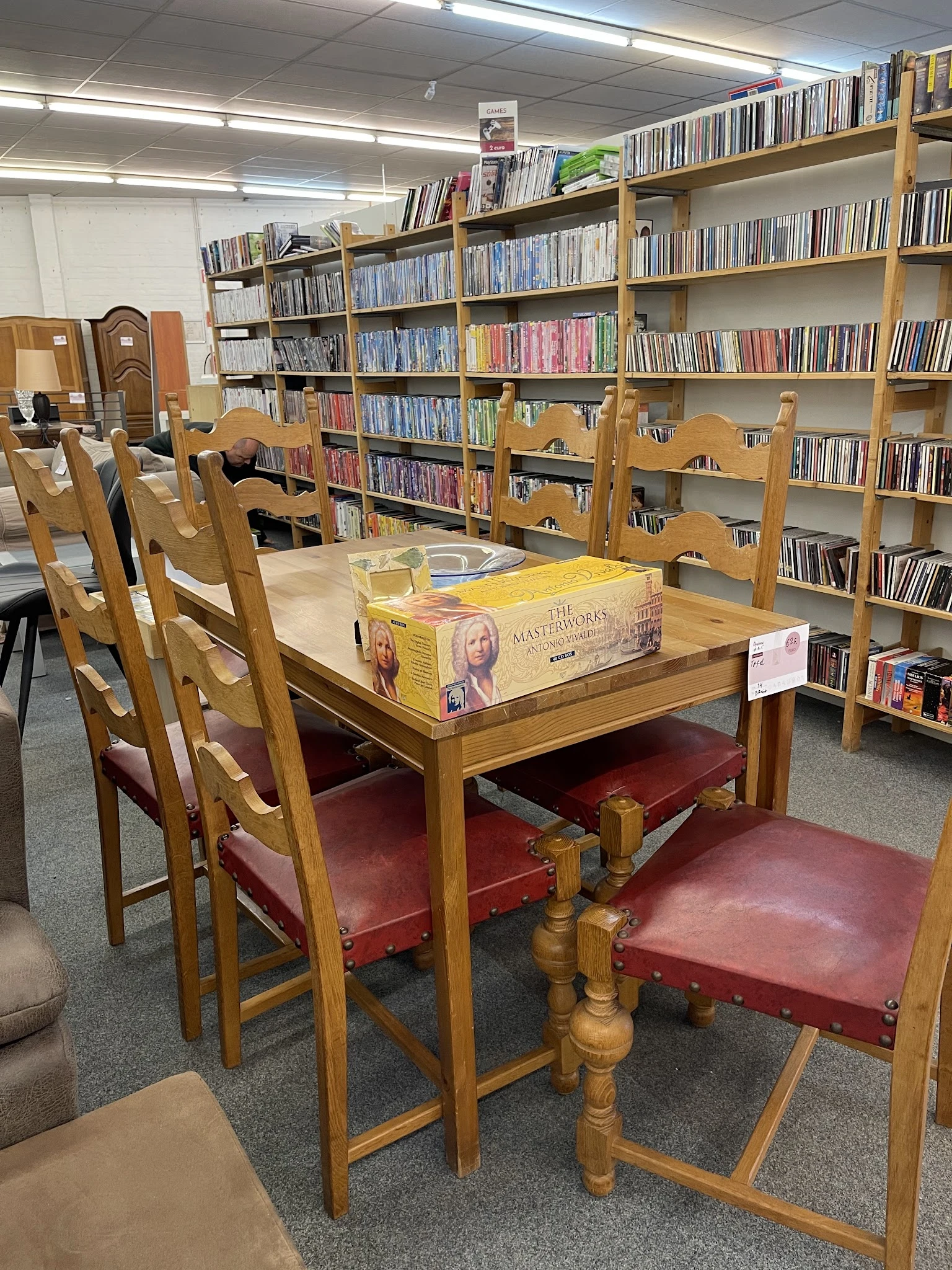 Leeszaal met houten tafel, stoelen met rode zitting en boekenkasten vol cd's en boeken op de achtergrond
