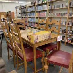 Leeszaal met houten tafel, stoelen met rode zitting en boekenkasten vol cd's en boeken op de achtergrond