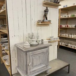 Uitgestalde serviesgoed en huishoudartikelen in een kringloopwinkel, met houten kastje, borden, kopjes en decorstukken