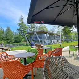Terras met oranje stoelen onder parasol, uitzicht op speeltuin en gebouwen