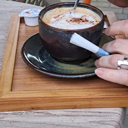 Close-up van een donkere keramische kop met schotelrand en cacao-drank, hand markeert onderkant met pen