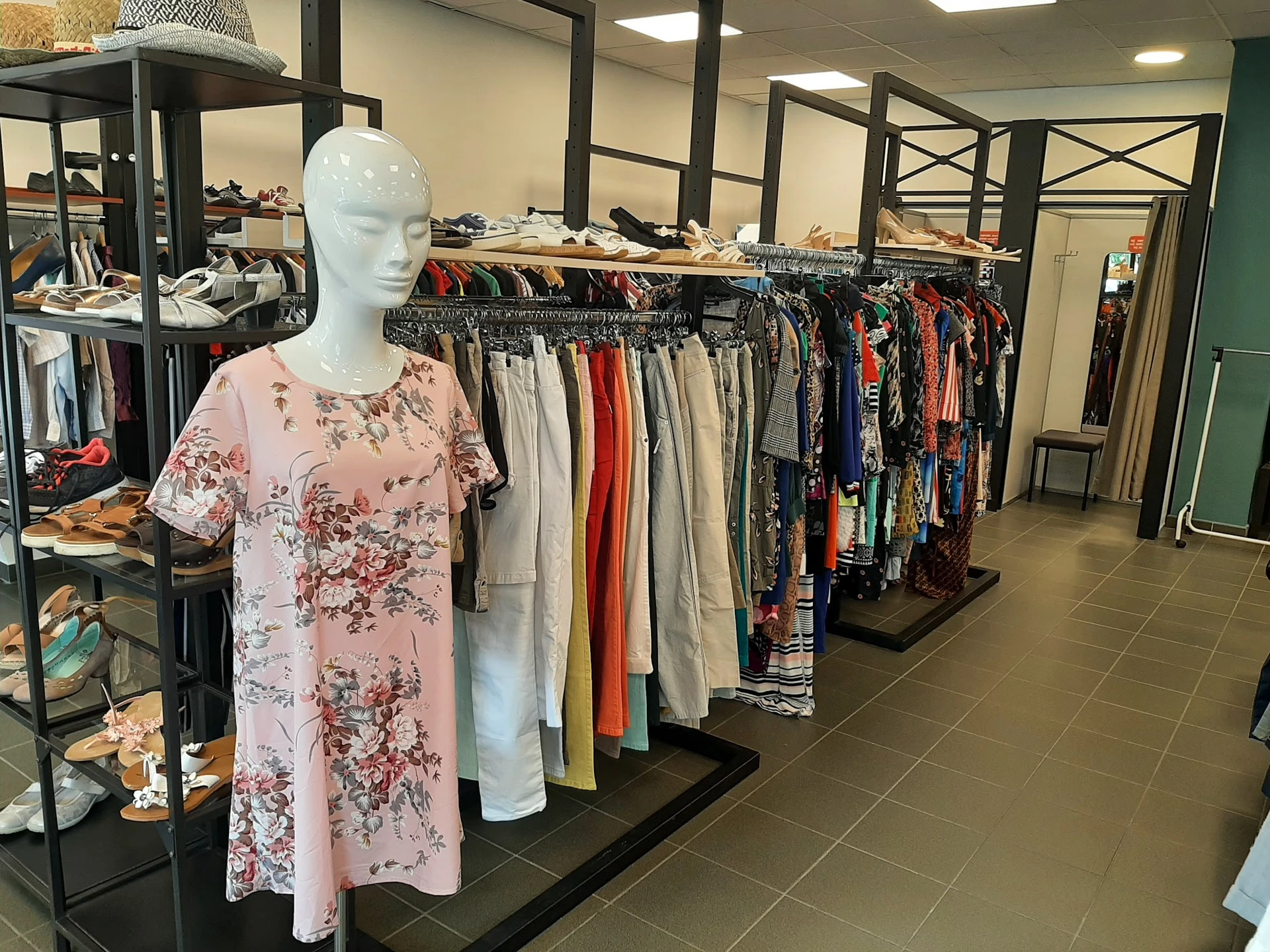 Mannequin met roze bloemenprint jurk tussen rekken met tweedehands kleding in kringloopwinkel