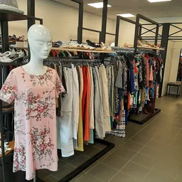 Mannequin met roze bloemenprint jurk tussen rekken met tweedehands kleding in kringloopwinkel