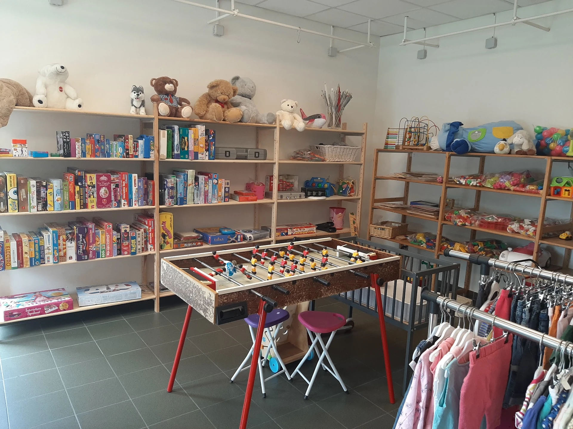 Winkelbinnenkant met boekenrekken, speelgoed, kinderkledingrek en een tafelvoetbalspel