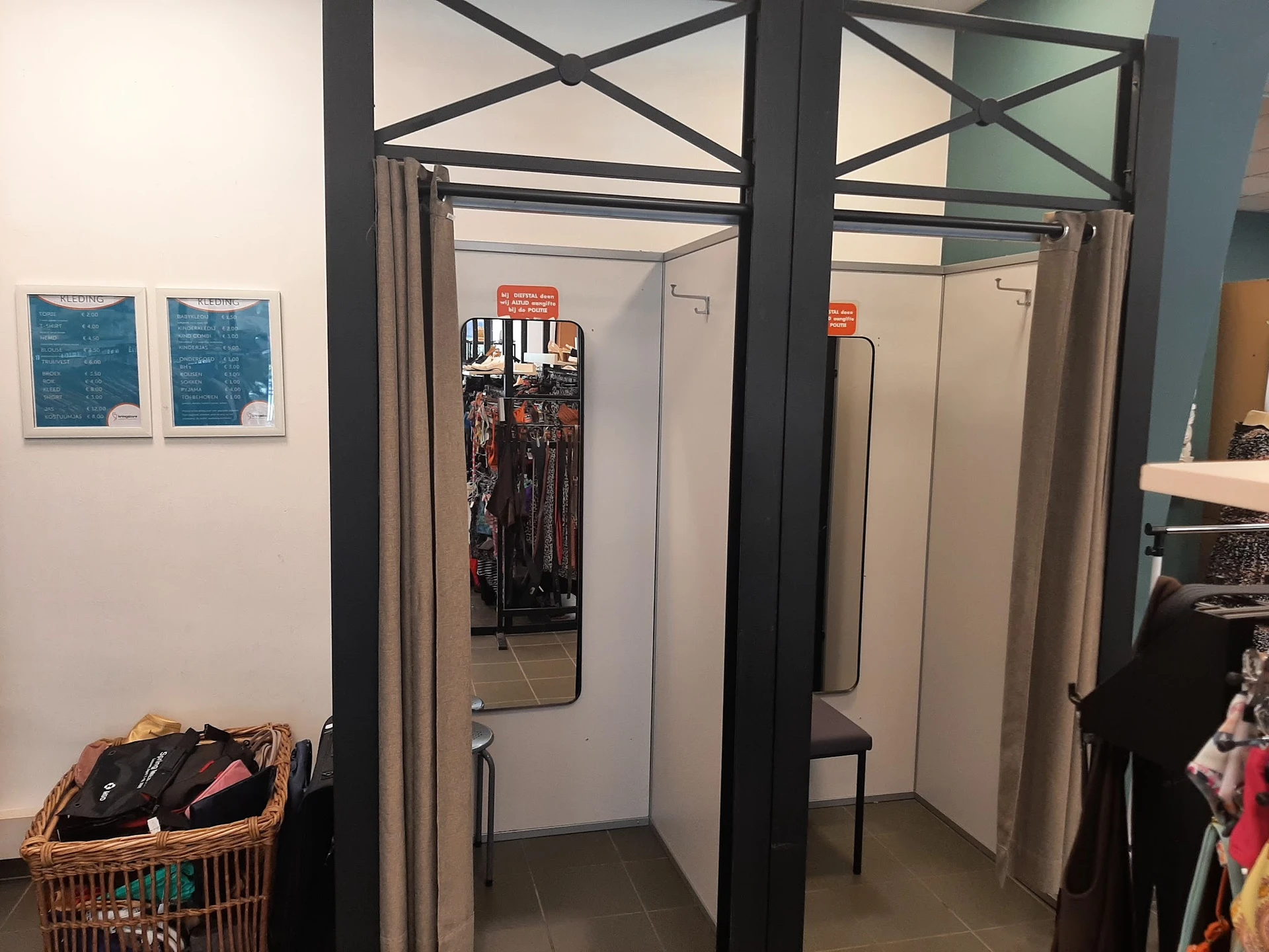 Paskamers met gordijnen en spiegels in een kringloopwinkel, daarnaast een mandje met kleding