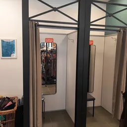 Paskamers met gordijnen en spiegels in een kringloopwinkel, daarnaast een mandje met kleding