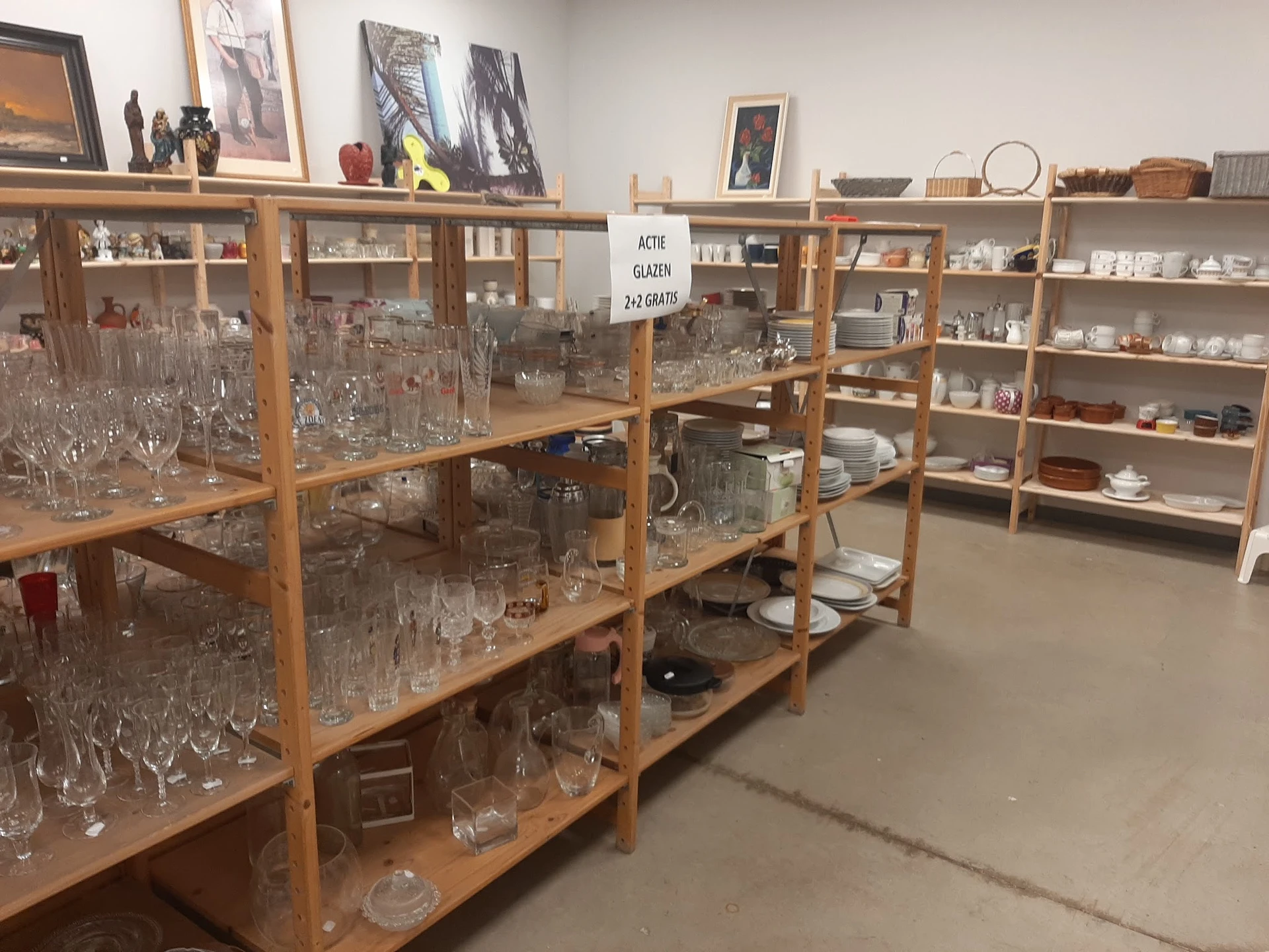Houten vitrinekasten met glaswerk, servies en decoratieve artikelen in kringloopwinkel