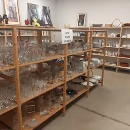 Houten vitrinekasten met glaswerk, servies en decoratieve artikelen in kringloopwinkel