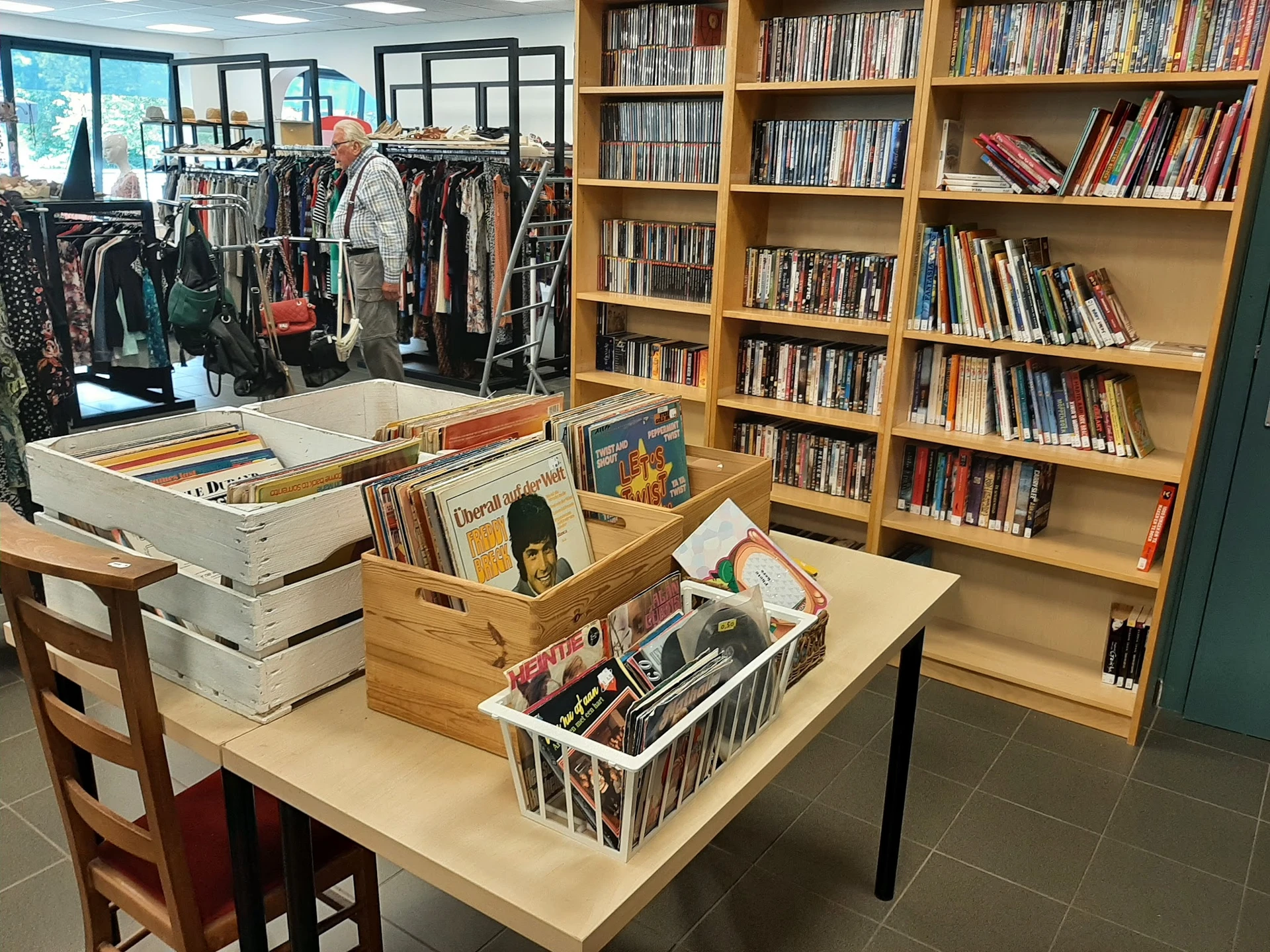 Winkelinterieur met boekenkasten, kledingrek en tafels met diverse tweedehands artikelen