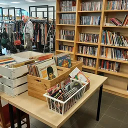 Winkelinterieur met boekenkasten, kledingrek en tafels met diverse tweedehands artikelen