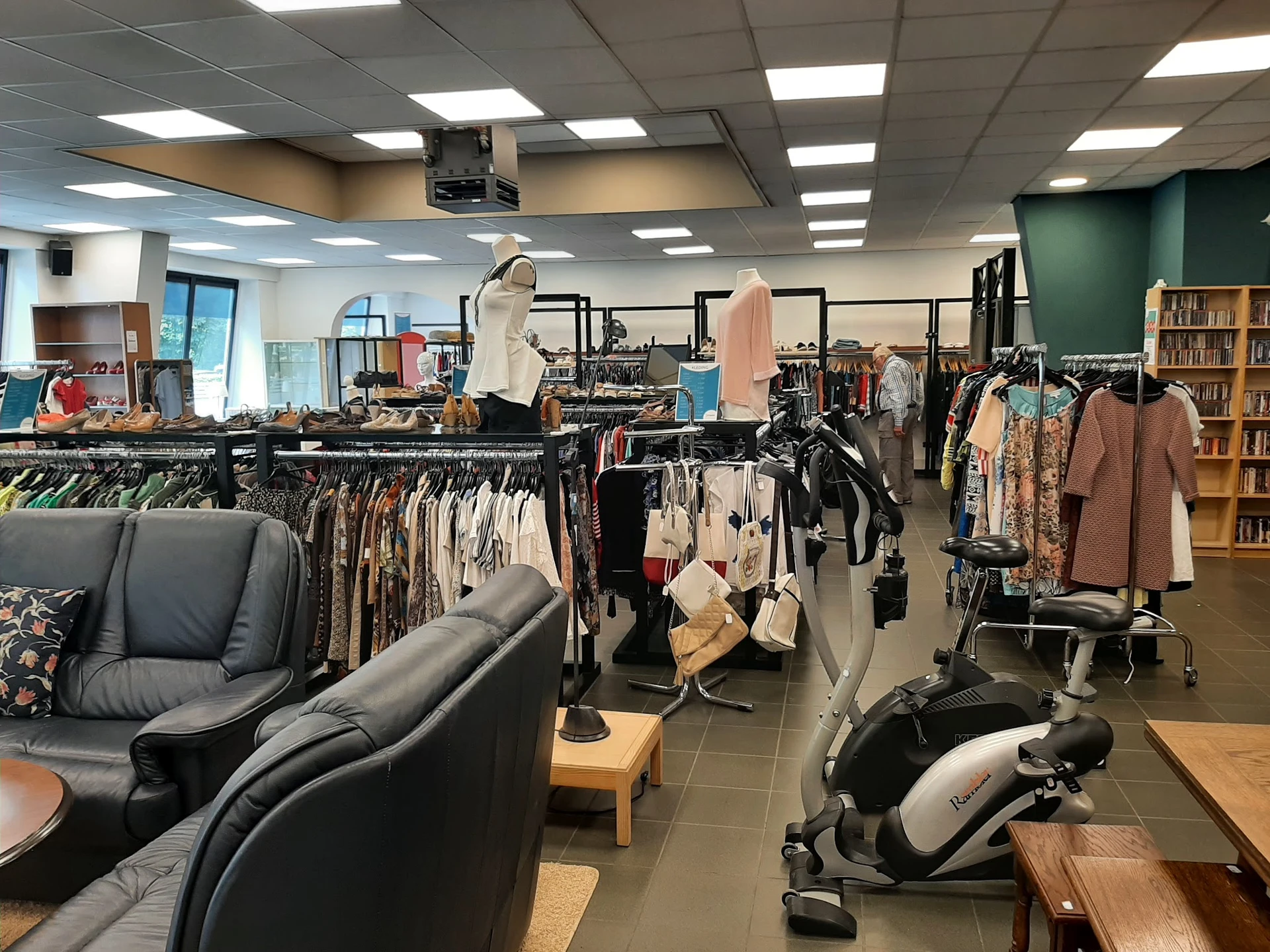 Winkelvloer met kledingrekken, fauteuils, boekenkast en fitnessequipment in tweedehands winkel