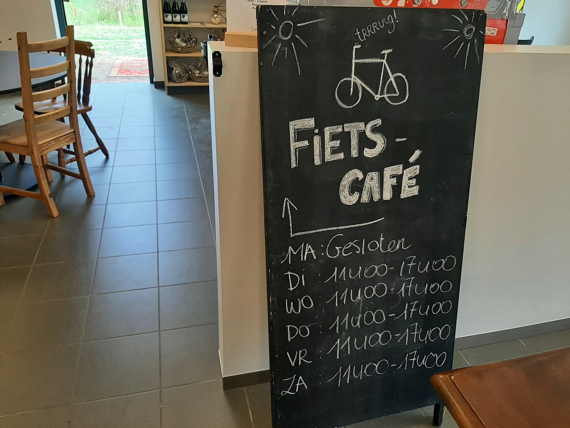Krijtbord met 'FIETS-CAFÉ' en openingsuren, fietsafbeelding, winkelvloer op achtergrond