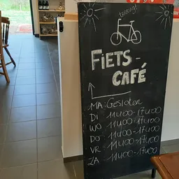 Krijtbord met 'FIETS-CAFÉ' en openingsuren, fietsafbeelding, winkelvloer op achtergrond