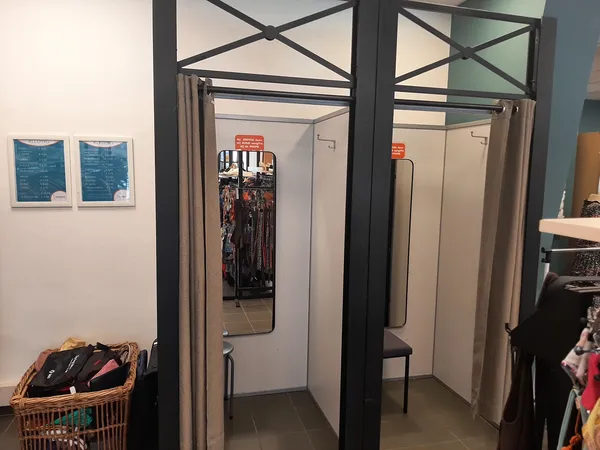 Kledingpaskamers met beige gordijnen en zwarte frames in een kringloopwinkel