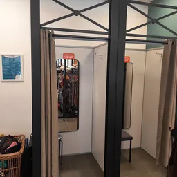 Kledingpaskamers met beige gordijnen en zwarte frames in een kringloopwinkel