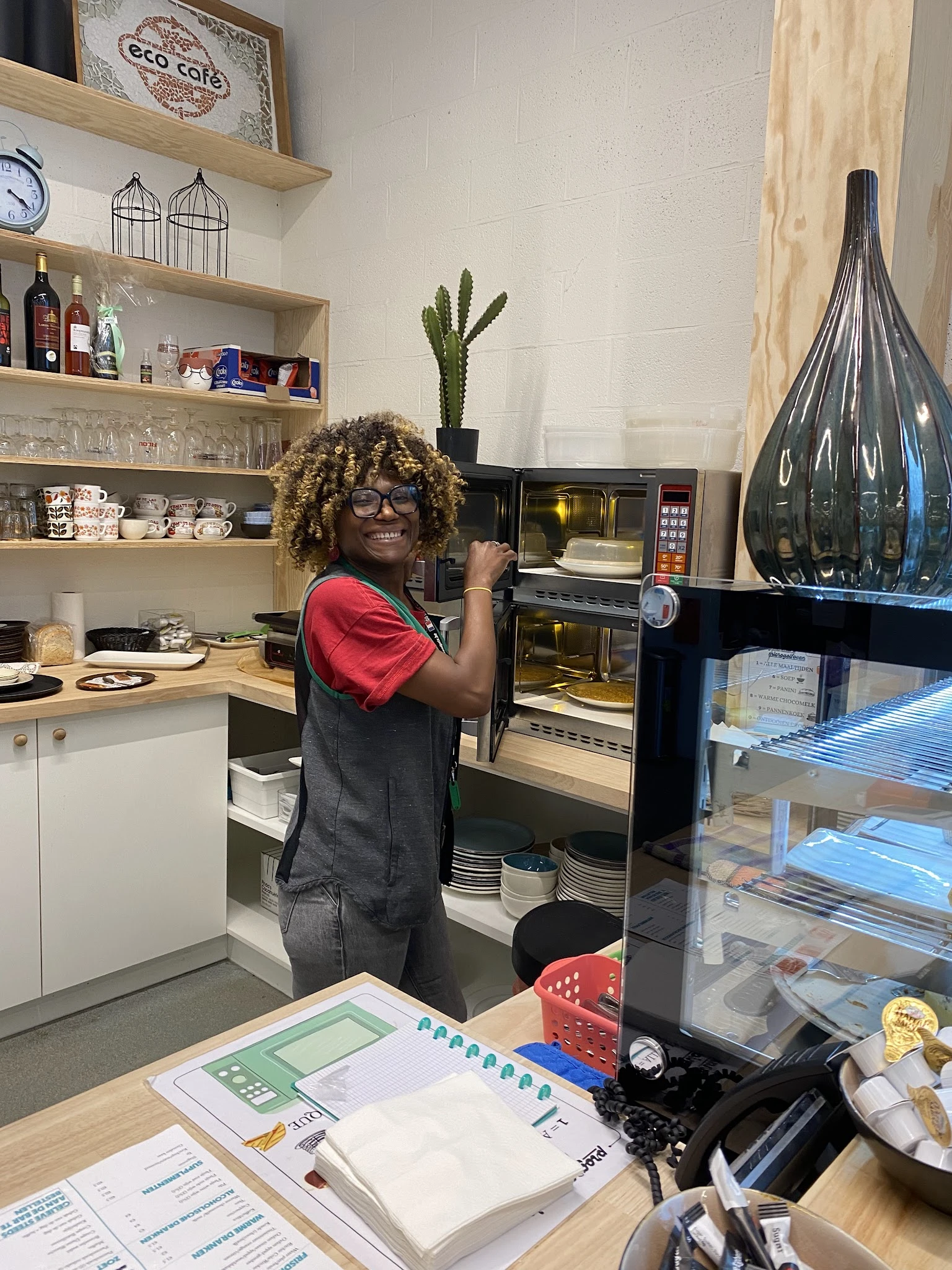 Medewerker in rode shirt en schort poseert bij professionele ovens in de keuken