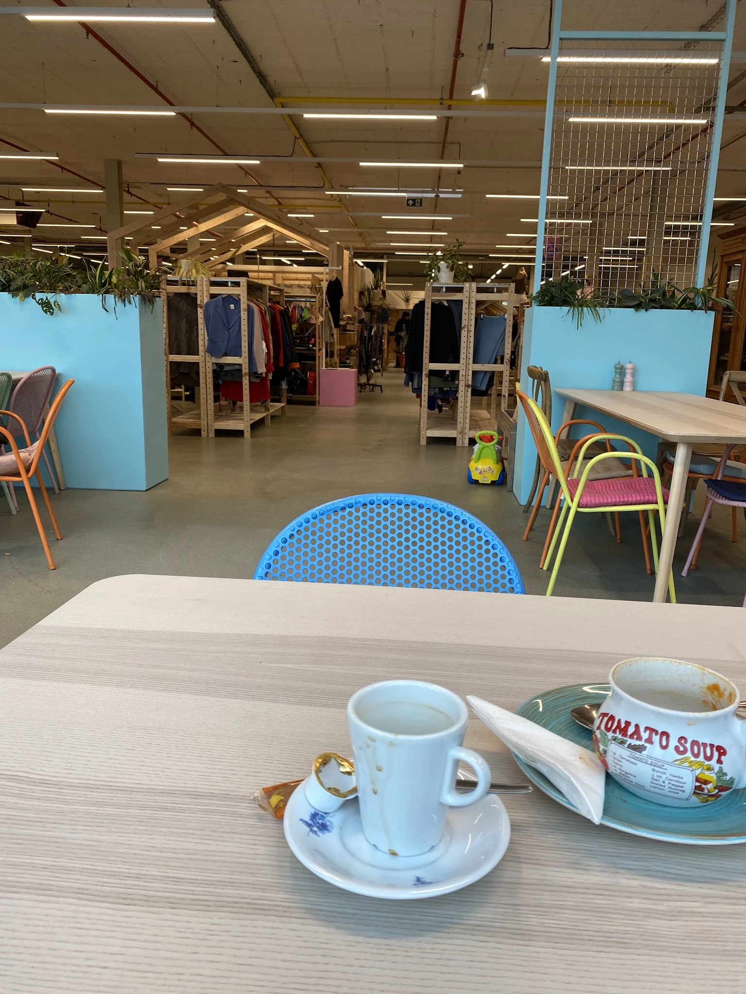 Tafel met kopjes koffie en een kom tomatensoep in een kringloopwinkel met zithoek