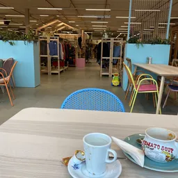 Tafel met kopjes koffie en een kom tomatensoep in een kringloopwinkel met zithoek