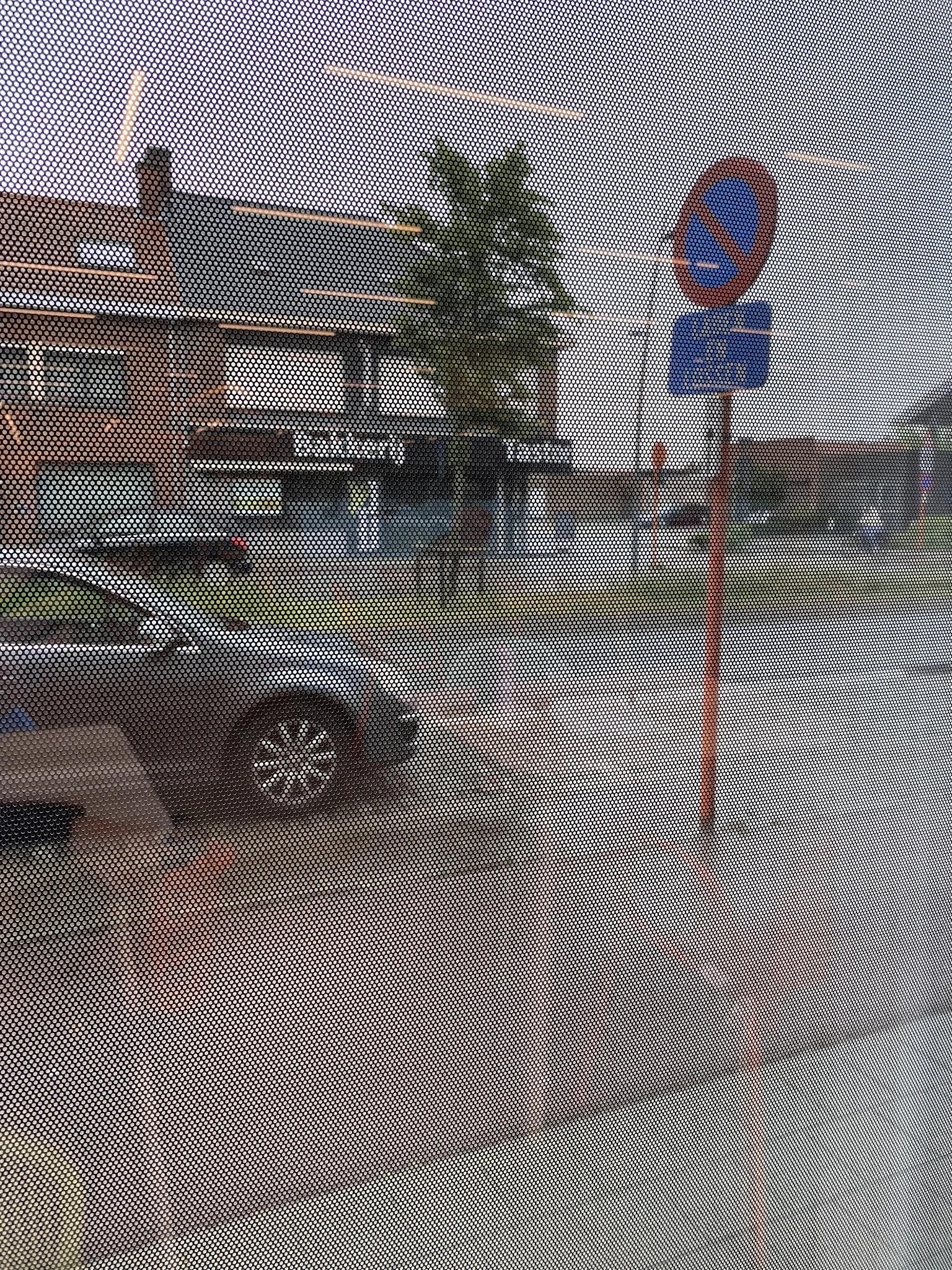 Voorkant van kringloopwinkel achter gaas, met parkeerplaats en rode paal zichtbaar