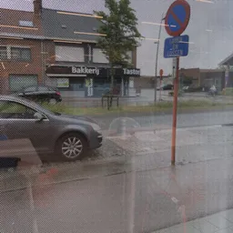 Voorkant van kringloopwinkel achter gaas, met parkeerplaats en rode paal zichtbaar