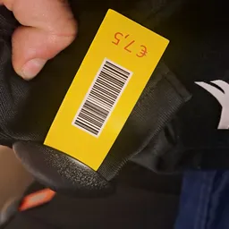 Gele prijssticker met code SL3 en barcode op donkere textielstof