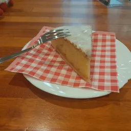 Een stuk cake met witte glazuur op een bord met rood-wit geblokt papier en vork