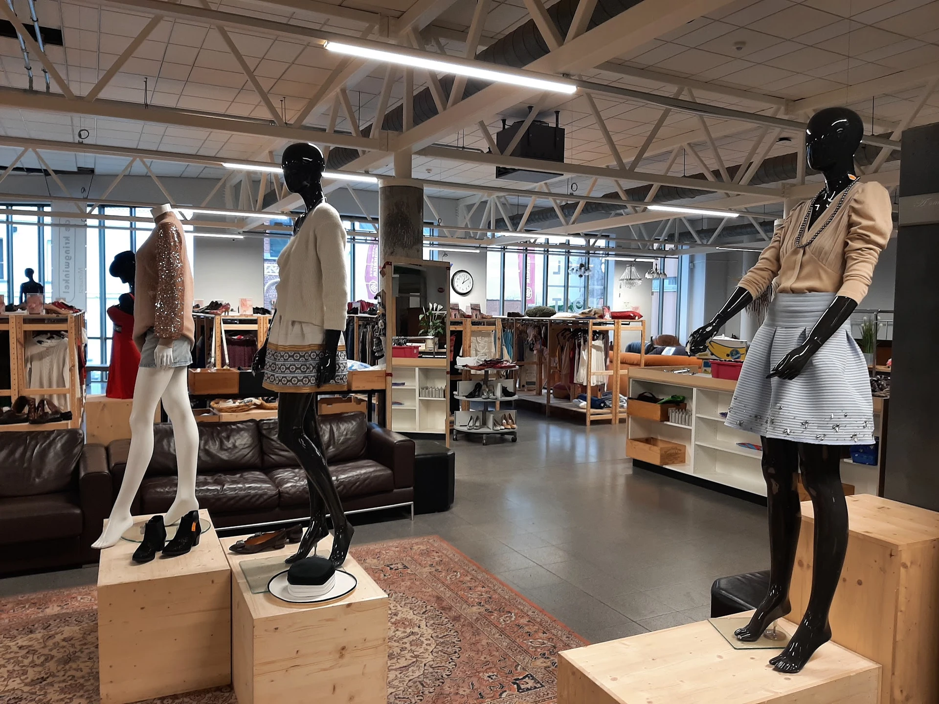 Ruime winkelruimte met mannequins in kledij, wooden displays, leather couch en diverse winkelrekken met tweedehands kleding