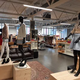 Ruime winkelruimte met mannequins in kledij, wooden displays, leather couch en diverse winkelrekken met tweedehands kleding