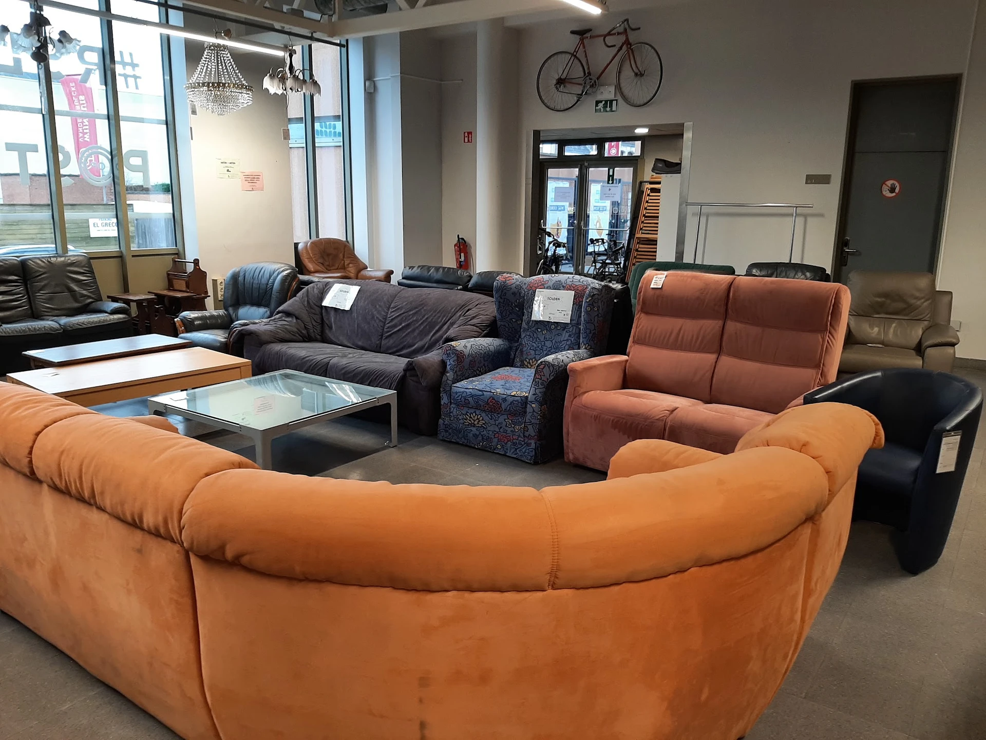 Winkelvloer met diverse zitmeubels: oranje en zwarte leren banken, grijze stoelen en fauteuils rond lage tafels