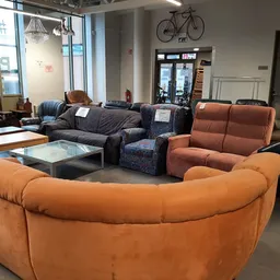 Winkelvloer met diverse zitmeubels: oranje en zwarte leren banken, grijze stoelen en fauteuils rond lage tafels