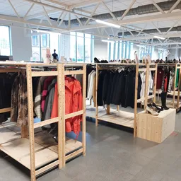 Houten kledingrekken met tweedehands jassen en kleding in een ruim magazijnachtige winkelruimte.