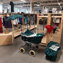 Uitgestalde tweedehands kleding op houten rekken en een kinderwagen met groene stof in een kringloopwinkel